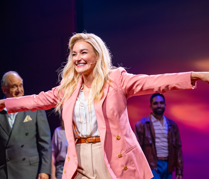 Betsy Wolfe bowing onstage in a pink suit