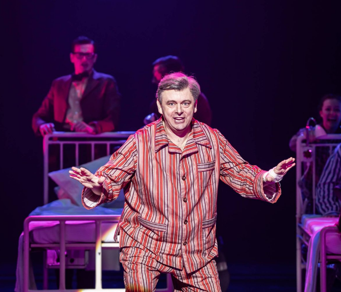 A man in striped pajamas standing in front of hospital beds talking