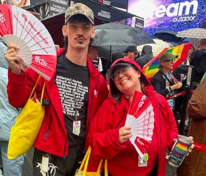 Two TKTS Patron Services Reps posting with TKTS fans by the booth