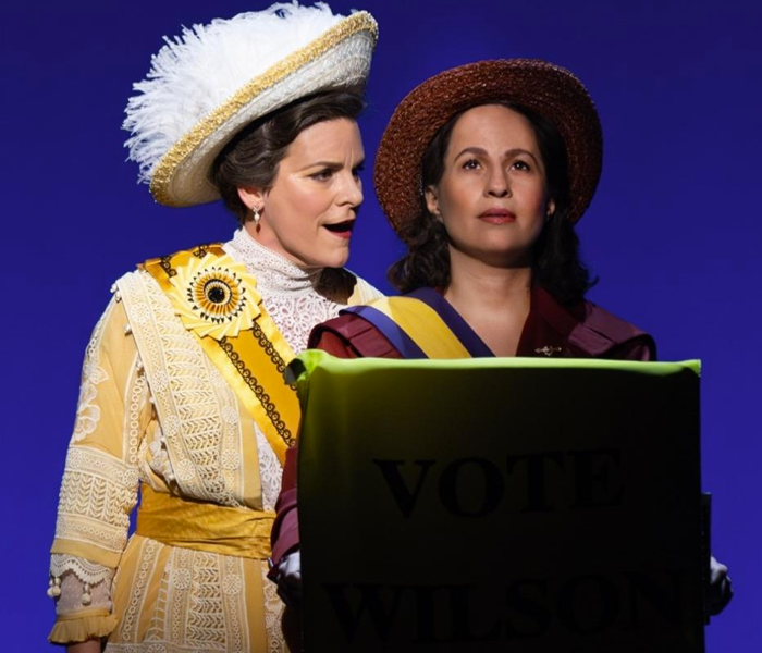 Two women in early 20th century costumes at a podium speaking
